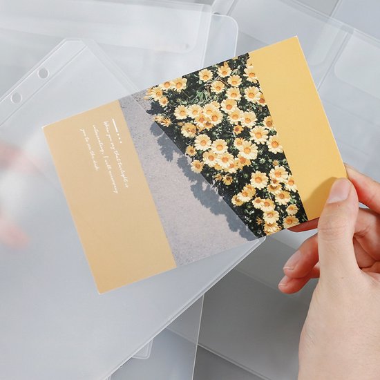 Hand houdt een ansichtkaart met gele bloemen en tekst vast, boven transparante insteekhoezen.
