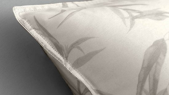 Een detail van een kussensloop met een licht beige kleur en een grijs patroon van bladeren.