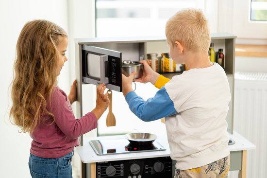 Kinderen spelen met een speelkeuken. Meisje opent magnetron, jongen pakt potje.