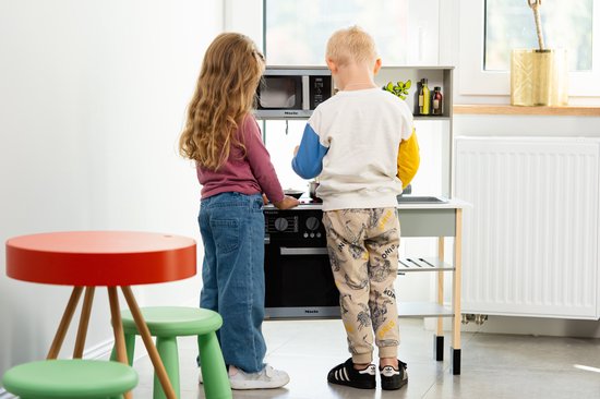 Kinderen spelen met een houten speelkeuken met magnetron, fornuis en gootsteen.