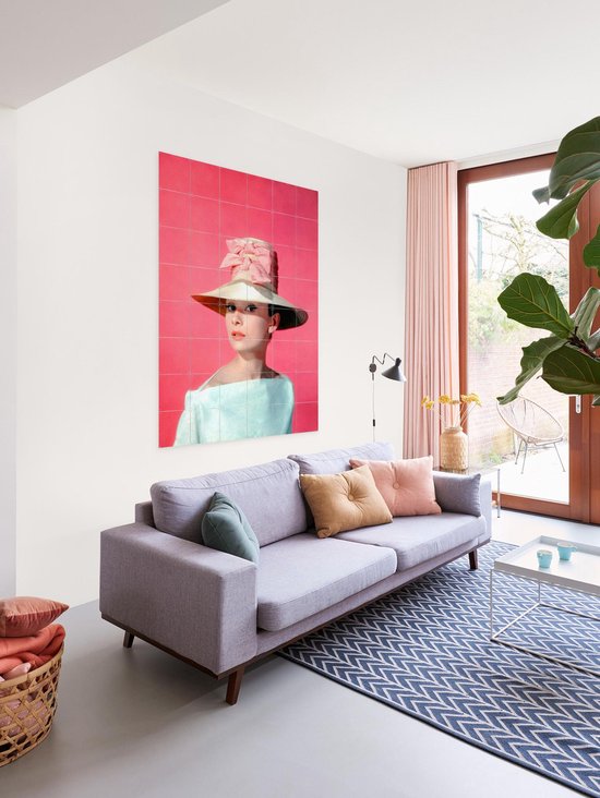 Audrey Hepburn portant un grand chapeau avec un nœud rose, suspendu au-dessus d'un canapé.