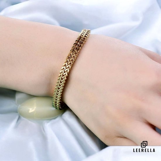 Gouden schakelarmband met dubbele rij schakels gedragen om een vrouwenpols, met witte stof.