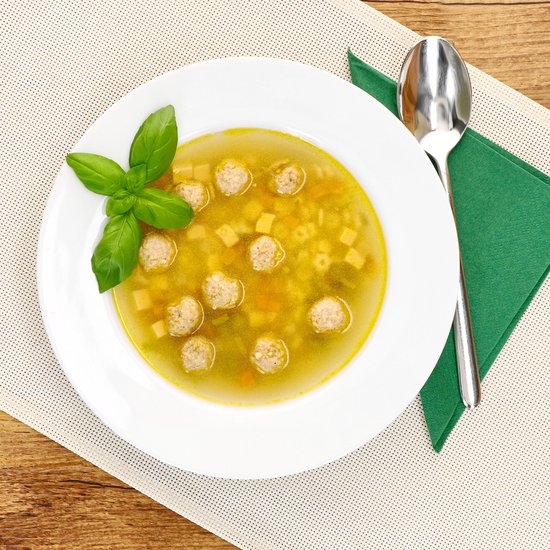 Witte soepkom met bouillon, gehaktballetjes, pasta en basilicum.