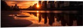 PVC Schuimplaat - Zon Verdwijnend tussen Wolkenkrabbers aan het Water - 150x50 cm Foto op PVC Schuimplaat (Met Ophangsysteem)