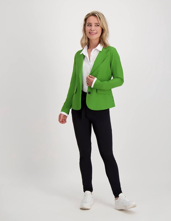Model draagt een felgroene blazer over een witte blouse, met een zwarte broek en witte sneakers.