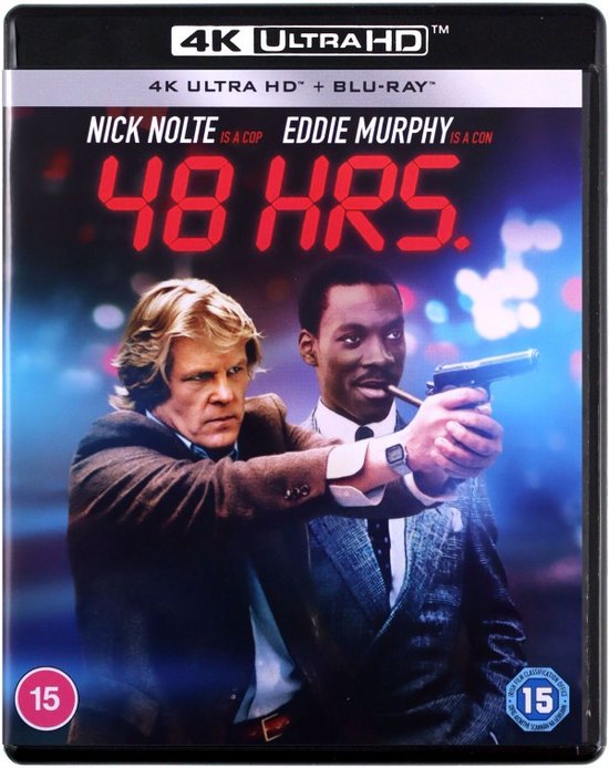 Nick Nolte en Eddie Murphy staan naast elkaar. Nolte draagt een bruin jasje, Murphy een grijs gestreept pak en houdt een pistool vast.