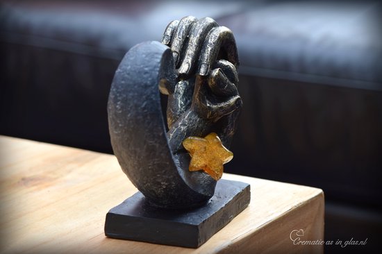 Zwarte hartvormige urn met gouden handen, met een amberkleurige glazen ster.