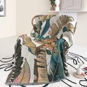 Beige deken met botanische print van bladeren, gedrapeerd over een stoel.
