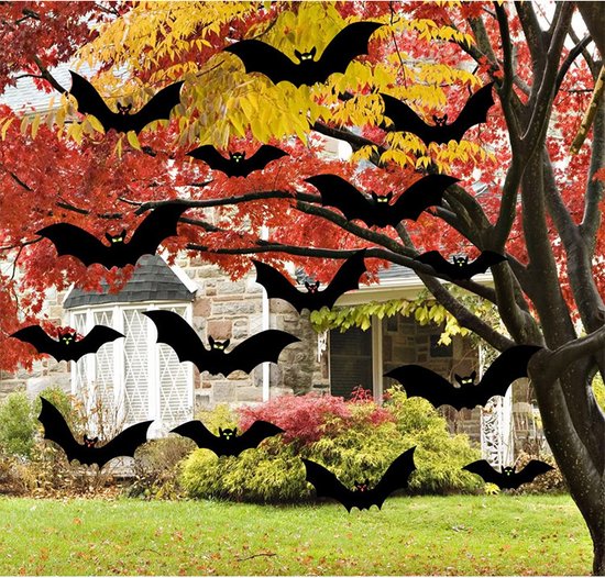 Zwarte vleermuisdecoraties hangen aan de takken van bomen met herfstbladeren, met een huis op de achtergrond.