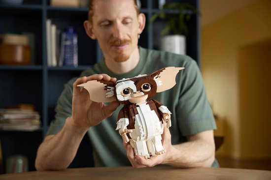 Een man met rood haar inspecteert een LEGO Ideas Gizmo figuur. Het figuur is bruin en wit, heeft grote oren en een vriendelijke uitdrukking.