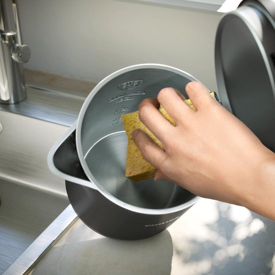 Een hand reinigt de roestvrijstalen binnenkant van een zwarte waterkoker met een spons.