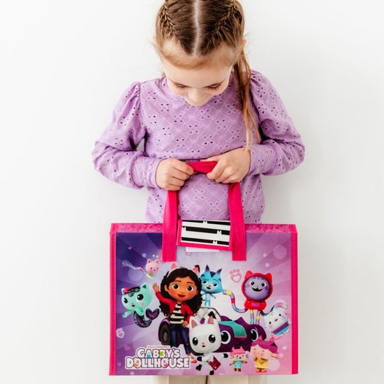 Een meisje in paarse trui kijkt naar een roze tas met Gabby's Poppenhuis personages, waaronder Gabby en haar katten.