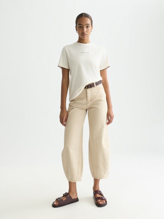 Le mannequin porte un t-shirt blanc cassé avec 'Cosmic Spirit' brodé sur la poitrine et un pantalon beige.