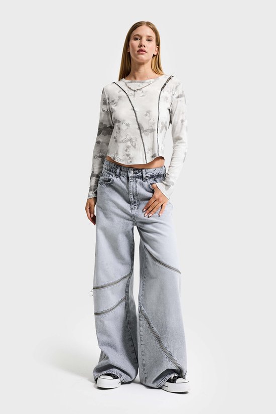 Model in een lichtgrijze baggy jeans met ritsdetails en een crop top.