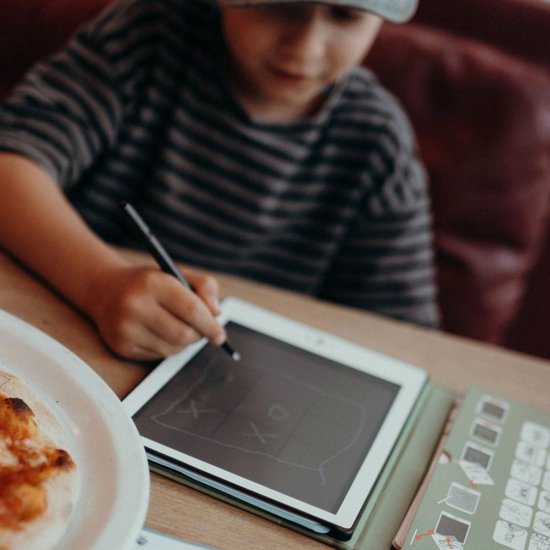 Kind met gestreepte trui tekent met stylus op een tablet.