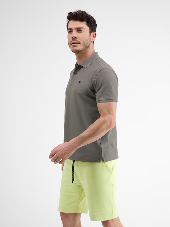 Man in donkergrijs poloshirt en lichtgroene korte broek, zicht van opzij.