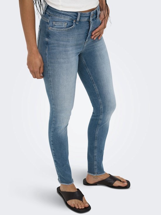 Model in een blauwe skinny fit jeans met middelhoge taille, rafels aan de zoom en zwarte sandalen.