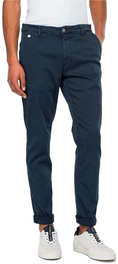 Man met donkerblauwe chino broek met omgeslagen broekspijpen en witte sneakers.