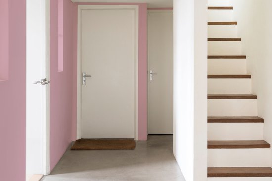 Hal met roze muur, witte deuren en houten trap.