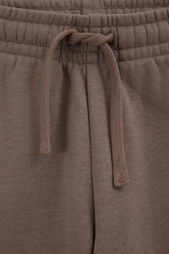 Detail van de tailleband van een bruine joggingbroek met trekkoord.