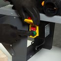 Handen met zwarte handschoenen drukken op de rode noodstop en groene aan/uit knop van de freestafel.