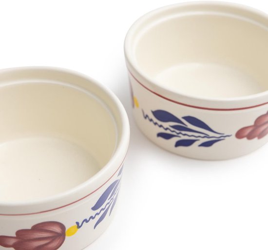 Twee crème ramkinkjes met rode en blauwe bloemen en bladeren decoratie.