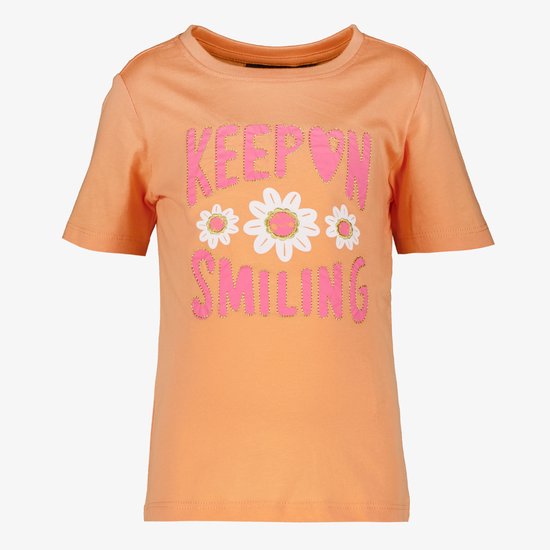 Oranje T-shirt met korte mouwen en de tekst 'KEEP ON SMILING' met bloemenprint, op een grijze achtergrond.