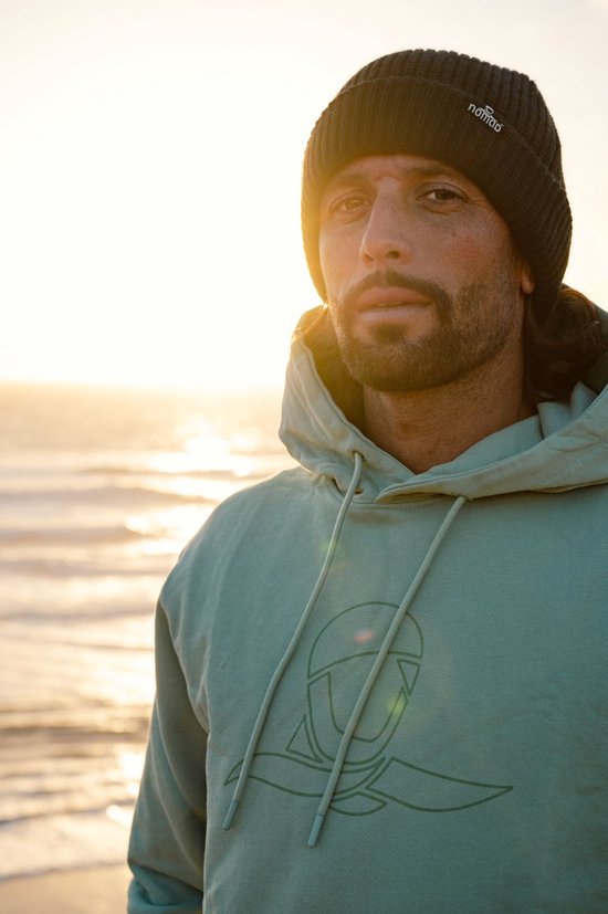 Man draagt mintgroene hoodie met logo en donkergrijze Nomad-muts bij zonsondergang.