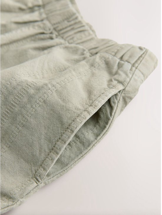 Detail van de zak van een lichtgroene broek met verticale textuur en elastische taille.