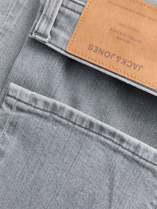 Grijze jeans met een bruin leren label van Jack & Jones met tekst.