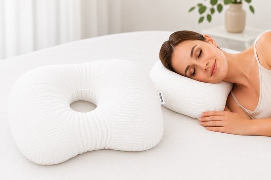 Een vrouw ligt te slapen op een wit kussen met een donutvormig kussen ernaast.