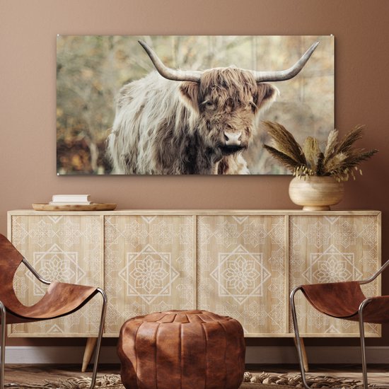 Woonkamer met een glasschilderij van een Schotse Hooglander boven een houten dressoir met bewerkte deuren.