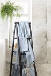 Lichtblauwe handdoeken hangen te drogen aan een donkere ladder in een badkamer met planten.