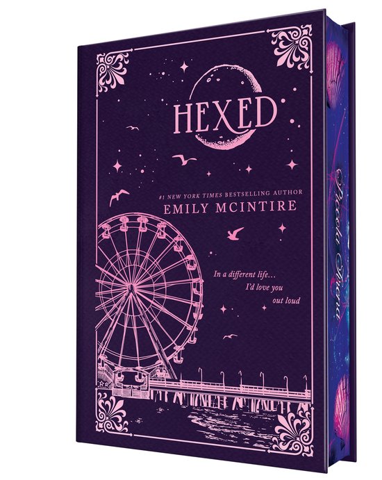 Édition reliée bleu foncé de 'Hexed' avec des illustrations roses d'une grande roue, d'une jetée et d'un ciel étoilé. Texte: 'HEXED', '#1 NEW YORK TIMES BESTSELLING AUTHOR EMILY MCINTIRE'.