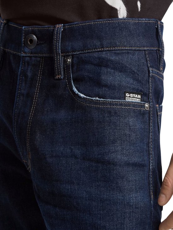 Close-up van de tailleband van een donkerblauwe G-Star jeans met knoop en het G-Star Originals label.