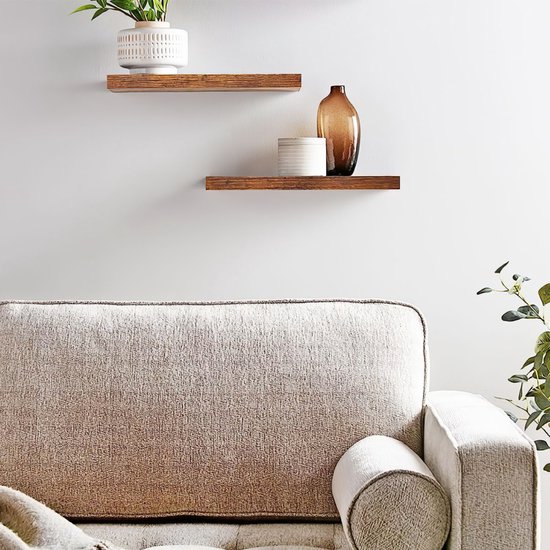 Twee zwevende donkerbruine houten planken aan een muur boven een bank, met een vaas en plant.