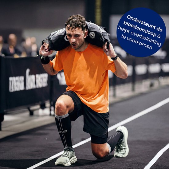Man met een oranje shirt en zwarte short die een zware tas draagt op zijn schouders, knielend met zwarte compressiekousen.