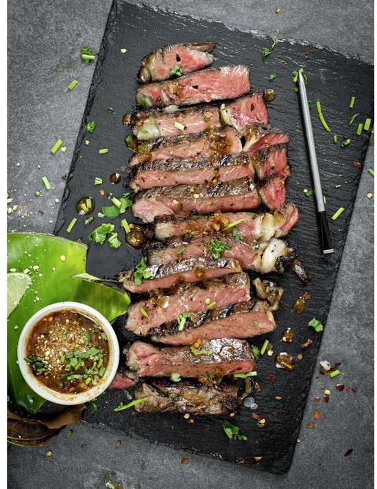 Gesneden entrecôte op een zwarte leisteen, met kruiden, dip en een Meater thermometer.