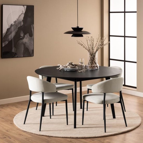 Een ronde, zwarte eettafel met vier lichte stoelen en een beige vloerkleed in een woonkamer.
