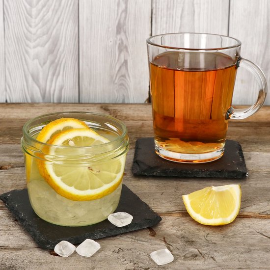 Glazen pot met water, citroenschijfjes en ijsblokjes, met een mok thee ernaast.