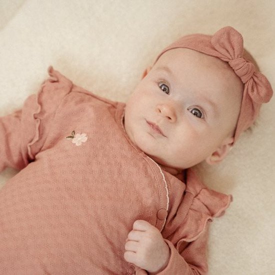 Baby met roze pakje met bloem en bijpassende haarband met strik.