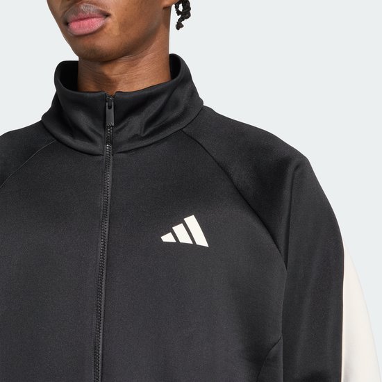 Close-up van de hoge kraag en ritssluiting van een zwarte jas met een wit adidas logo op de borst.