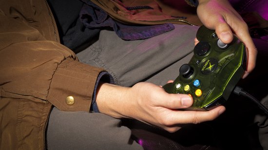 Dichtbij bekeken: handen houden een doorzichtige groene Xbox controller vast. De controller heeft kleurrijke knoppen.