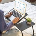 Een persoon gebruikt een laptop op de grijze gestreepte tafel. De tafel heeft een bekerhouder met een plantje.