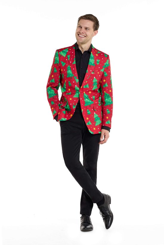 Man met rode kerstblazer met print van groene bomen en sterren, hand in zak, poseert.