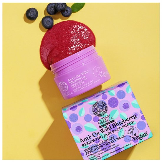 Paarse pot met 'Anti-Ox Wild Blueberry Renewing Jam Face Scrub', paarse doos met blauwe bessenprint, verse bosbessen en rode scrub.