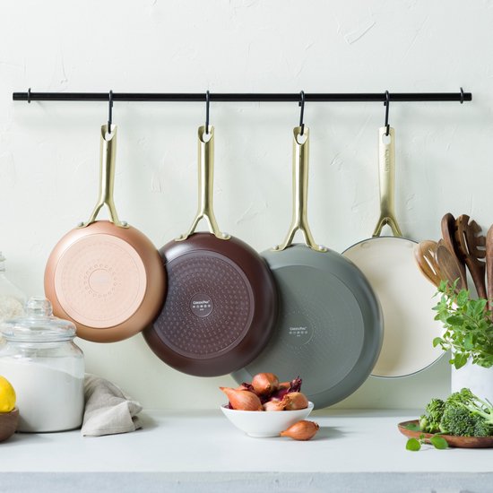 Vier koekenpannen met gouden handvatten hangen aan een rek. Kleuren: koper, bruin, grijs en crème.
