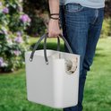 Man draagt een witte afvalbak met twee vakken en donkergrijze hengsels in een tuin.
