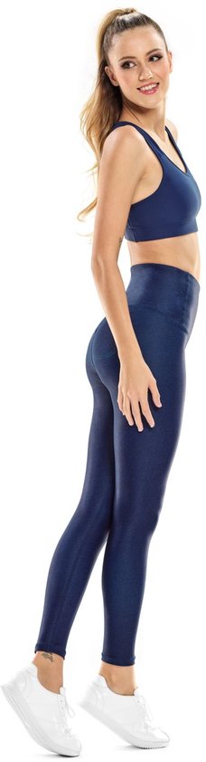 Zijaanzicht van model in donkerblauwe sportbeha en glimmende legging, met witte sportschoenen.