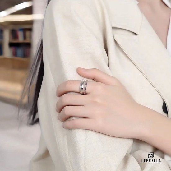 Vrouw met zilverkleurige ring met twee banden aan haar gekruiste arm, gedragen op de wijsvinger.